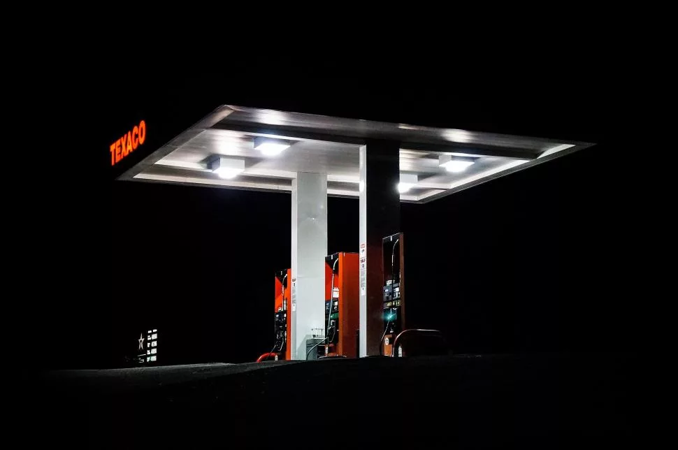 A Gas Station Is Brightly Lit Up At Night, With Its Lights Casting A Glow On The Surrounding Area.
