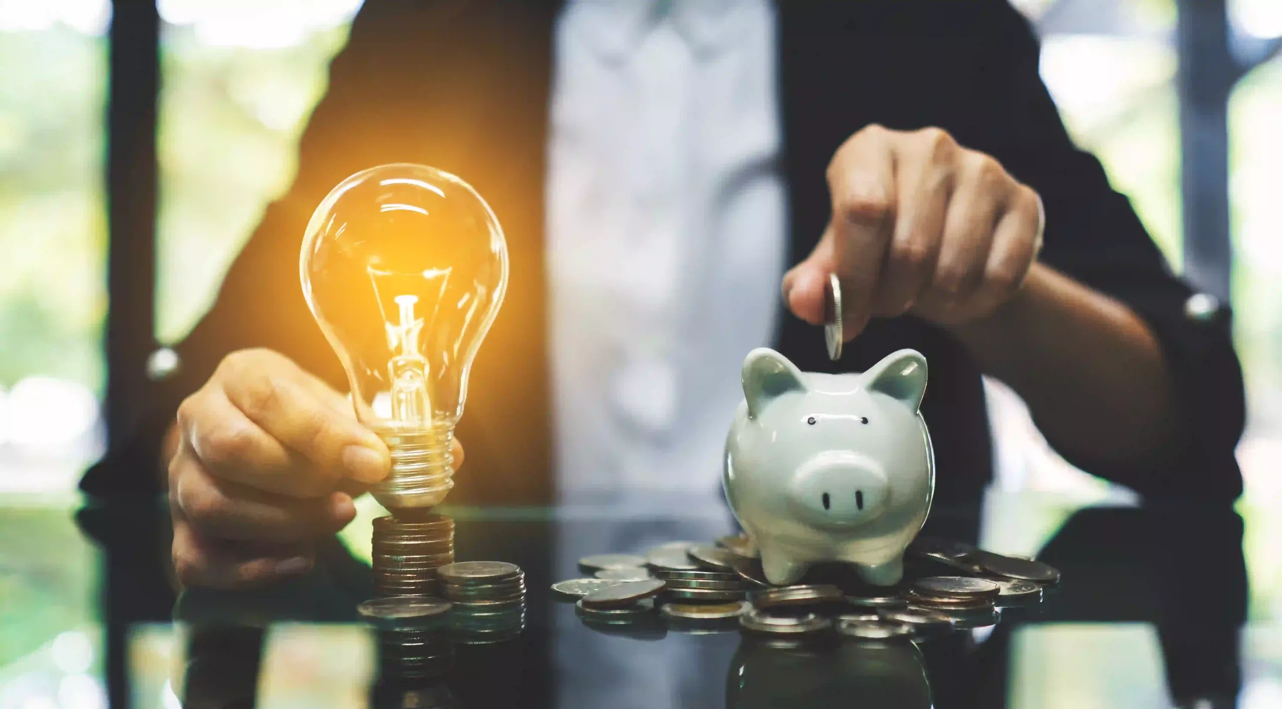 A Businesswoman Putting Coin Into Piggy Bank And A Light Bulb Over Coins Stack On The Table