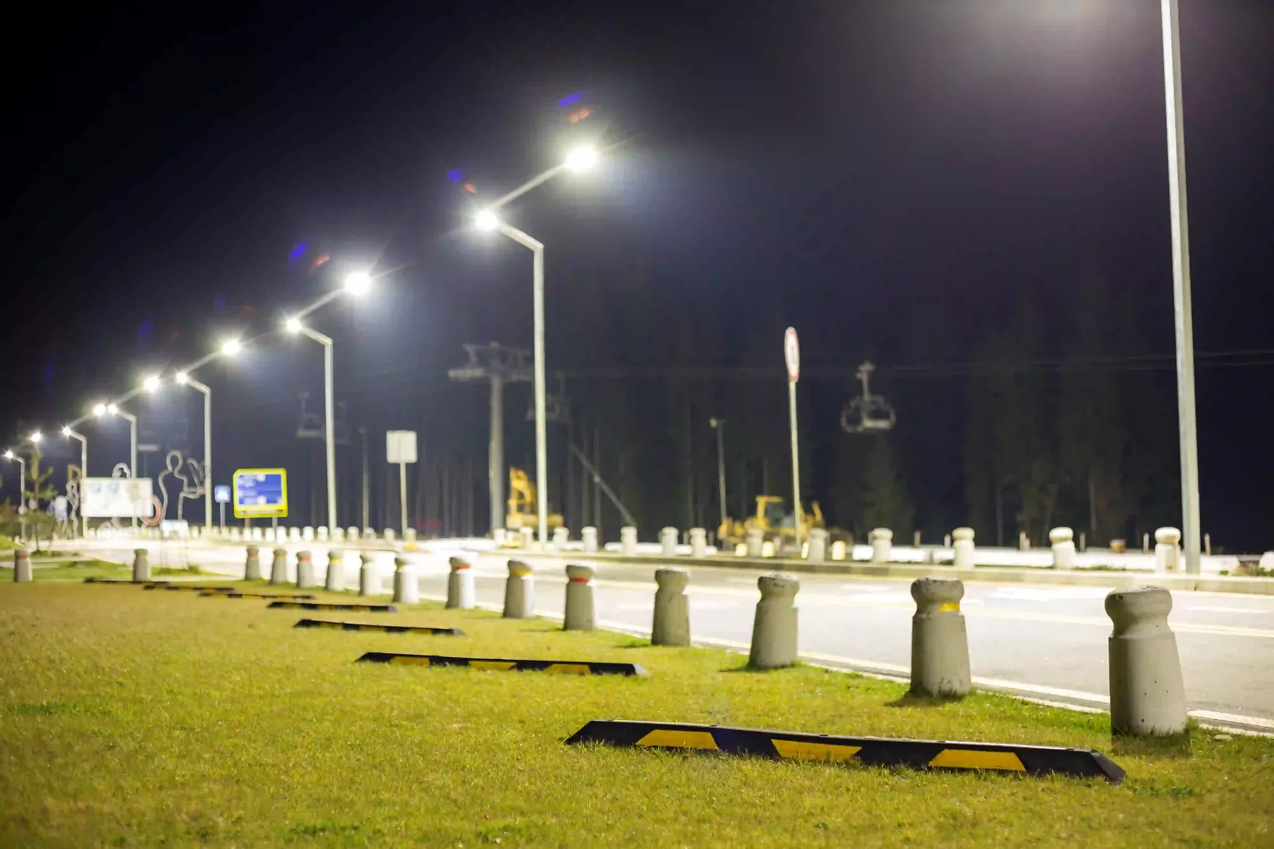 Empty Parking Lot On Green Lawn Brightly Illuminated By Street Lamps Along Road